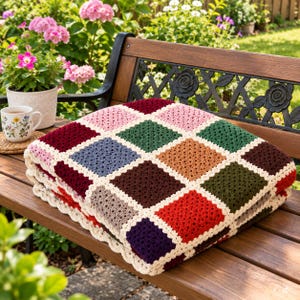 Puede incluir: Una manta tejida a ganchillo a mano con un patrón de cuadrados de la abuela multicolor en tonos burdeos, verde bosque, amarillo mostaza, azul marino, rosa claro y marrón oscuro, unidos por un borde color crema con un acabado festoneado.