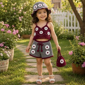May include: A crochet set consisting of a dark red crop top with white daisy motifs, grey shorts with white daisy motifs and a dark red drawstring, a matching grey bucket hat with white daisy motifs, and a small dark red crochet handbag.
