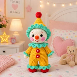 May include: A handmade crochet clown doll featuring a yellow body, a matching pointed hat with a red pom-pom, and teal ruffled accents at the neck, wrists, and ankles. The doll has a white face, black eyes, a red nose, and pink cheeks.