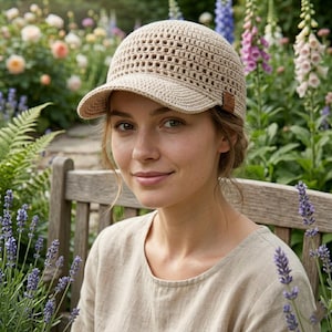 May include: A beige crochet baseball cap featuring an open-weave pattern on the crown and a solid, tightly stitched brim. A small, rectangular brown leather-like tag with a logo is attached to the side of the cap near the brim edge.