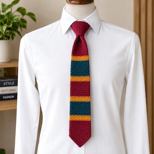 Puede incluir: Una camisa blanca de botones combinada con una corbata de punto con rayas horizontales en color burdeos, amarillo mostaza y azul cerceta oscuro. La corbata tiene una textura tejida con punta y un nudo estándar.