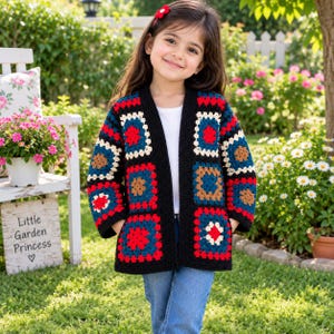 May include: A long-sleeve cardigan featuring a multi-coloured granny square crochet pattern in shades of red, blue, black, and cream. The garment has an open front design, long sleeves, and a black crocheted border along the edges and cuffs.