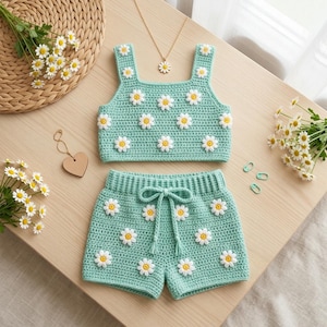 Può includere: Un completo in due pezzi all'uncinetto color verde menta composto da un top corto senza maniche e pantaloncini. Entrambi i capi presentano un motivo ripetuto di applicazioni a forma di margherita bianca con il centro giallo e un cordino.