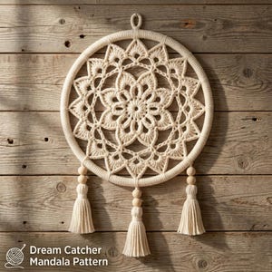 Puede incluir: Un adorno de pared circular de macramé color crema con un intrincado patrón de mandala de ganchillo dentro del aro. La pieza incluye tres borlas colgantes, cada una acentuada con dos cuentas de madera lisas, y un pequeño lazo para colgar.
