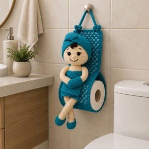 Peut inclure: Un porte-papier toilette en crochet représentant une poupée au teint beige, vêtue d'une serviette et d'un turban bleu sarcelle. La poupée est fixée sur un support en crochet bleu sarcelle à motifs de cœurs blancs pour maintenir le rouleau.