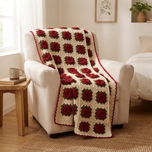 May include: A crochet blanket featuring a repeating pattern of square motifs, each containing a three-dimensional dark red rose surrounded by dark green leaves on a cream-colored background, finished with a scalloped dark red border edge.