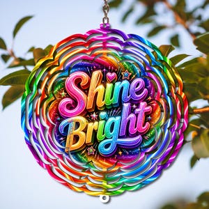 May include: A circular metal wind spinner featuring a vibrant rainbow-colored swirl pattern. The center displays the text "Shine Bright" in bold, multi-colored 3D lettering, accented by small star and heart shapes against a sparkling background.