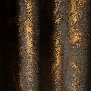 Pode incluir: Uma cortina de tecido cinza-escuro com um padrão abstrato em ouro metálico. O material tem uma superfície texturizada com dobras verticais que criam profundidade e sombra, destacando o contraste entre a base escura e a folha de ouro.