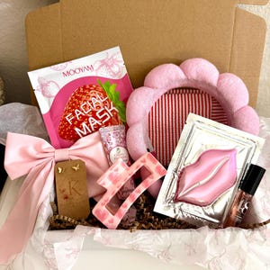 Puede incluir: Una caja de regalo que contiene una mascarilla facial de fresa Mooyam, una diadema rosa festoneada, una mascarilla para labios, una pinza para el cabello rosa con corazones, un lazo rosa claro, un tubo de crema de flor de cerezo y pendientes de mariposa dorados.