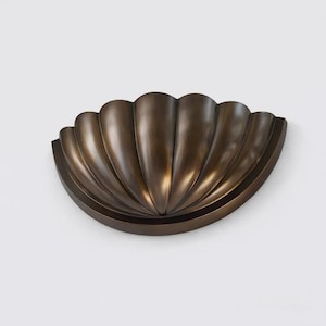 May include: A semi-circular wall light featuring a dark bronze finish and a scalloped shell design. The fixture has a series of vertical ridges radiating from the centre base, creating a textured, fan-like appearance with a smooth, curved edge.