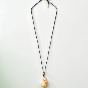 May include: A necklace featuring a single, spiraled, tan and white seashell pendant suspended from a thin, black cord. The cord includes a small, metallic gold-toned bead accent near the top closure, providing a simple and clean design.