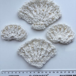 May include: Four white crocheted shell appliques decorated with small white beads. The largest shell measures approximately 9 cm wide, while the smaller shells vary in size. A ruler is visible at the bottom for scale reference.