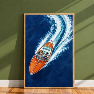 Op de afbeelding: Een verticale ingelijste kunstdruk met een houten speedboot die door diepblauw water vaart en een wit kielzog achterlaat. Twee figuren zitten in de boot, die aan de achtersteven is voorzien van een kleine Franse vlag.
