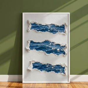 Puede incluir: Una pieza de arte mural rectangular con una superficie blanca texturizada y tres secciones horizontales rasgadas que revelan una escena de océano azul profundo con luz solar reflejándose en las ondas. Marco blanco delgado.