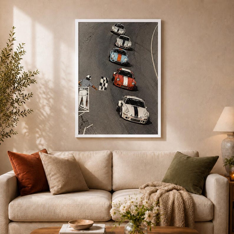 Pu&ograve; includere: Una stampa artistica da parete incorniciata che mostra una vista dall'alto di cinque auto sportive d'epoca su una pista. Un ufficiale di gara in camicia a righe tiene in mano una bandiera a scacchi. Le auto sono bianche, blu e rosse.