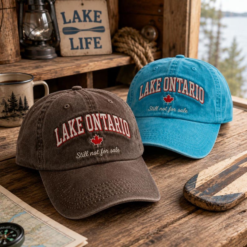 May include: Two baseball caps, one brown and one bright blue, each featuring the embroidered text LAKE ONTARIO in an arched font, a small red maple leaf icon, and the cursive script Still not for sale centered on the front panels.
