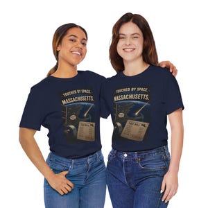 Könnte beinhalten: Ein marineblaues T-Shirt mit einem Grafikdruck der Erde aus dem Weltraum, einem Lichtstreifen und einer Steuerrechnung. Der Text lautet: TOUCHED BY SPACE, TAXED BY MASSACHUSETTS. Eine Sprechblase sagt WICKED COOL. Die Rechnung zeigt 1.990,00 $.