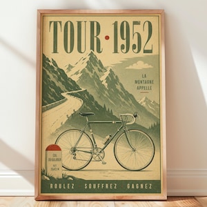 May include: A framed poster titled TOUR 1952 featuring a mountain landscape with a winding road, a road bicycle, and a milestone marker labeled COL DU GALIBIER ALT 2642 M. The text reads LA MONTAGNE APPELLE and ROULEZ SOUFFREZ GAGNEZ in a muted color palette.