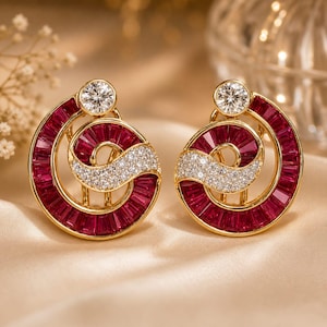 May include: A pair of gold earrings featuring a spiral design set with baguette-cut deep red rubies and small round white diamonds. Each earring includes a single larger round white diamond at the top of the spiral, creating a symmetrical look.