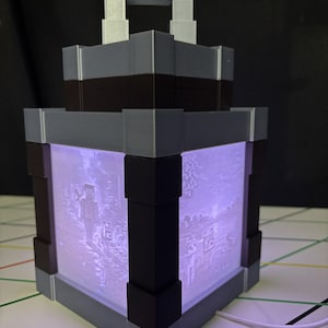May include: A square-shaped lantern with a blocky design featuring a gray and black frame. The translucent panels are illuminated with a purple light and display detailed pixelated scenes of characters and landscapes from a video game.