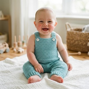 May include: A teal crochet romper featuring a square neckline, two white buttons on the shoulder straps, and a textured stitch pattern. The garment is sleeveless with a fitted bodice and short legs, providing a simple and functional design for infants.