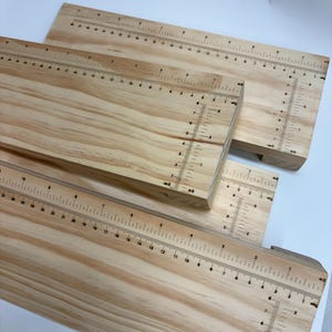 May include: Three rectangular light-colored wooden boards featuring printed black measurement scales along the edges. Each board displays numerical markings in centimeters, with horizontal and vertical rulers integrated into the wood surface.