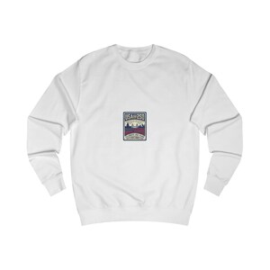 Peut inclure: Un sweat-shirt blanc à manches longues avec un motif rectangulaire sur la poitrine. Le graphique affiche le texte USA@250 et CELEBRATE 250 YEARS, ainsi qu'une illustration stylisée d'un pont, d'un bâtiment et un motif de drapeau rouge, blanc et bleu.