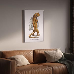 Può includere: Una stampa artistica da parete incorniciata che raffigura un geco color marrone chiaro e arancione che cammina portando sulla schiena una figura bianca simile a un fantasma. L'illustrazione include il testo Dr. Gecko & Mr. Fired Up.