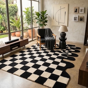May include: A rectangular area rug featuring a black and white chequered pattern that transitions into an irregular, fluid, wavy edge on one side. The rug is made of a textured material and covers a portion of the floor in a living space.