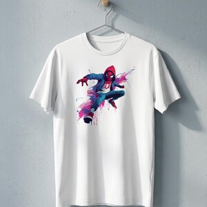 May include: A white short-sleeved t-shirt featuring a graphic print of a character wearing a red hooded jacket, blue pants, and red shoes, depicted in a dynamic pose with abstract blue and pink watercolor-style paint splatters surrounding them.