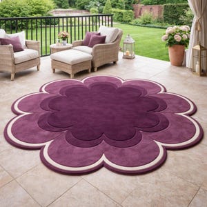Könnte beinhalten: Ein großer, runder Teppich in Blumenform mit mehreren überlappenden Blütenblättern. Der Teppich hat eine tiefviolette Mitte, einen helleren violetten Mittelteil und einen dünnen, cremefarbenen Rand, der die gesamte Blumenform umreißt.