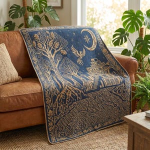 Puede incluir: Una manta tejida rectangular con un esquema de color azul oscuro y bronceado. El diseño muestra un árbol grande con raíces expuestas, un pájaro volando, una luna creciente con una estrella y una estructura de edificio de varios niveles sobre un patrón de laberinto.