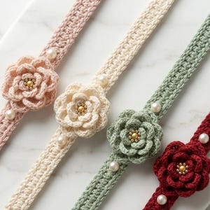 May include: Four crochet headbands in light pink, cream, sage green, and deep red. Each headband features a central crocheted flower with a gold bead center, flanked by two white faux pearls on the band. The bands have a textured, woven stitch.