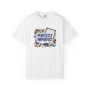 Peut inclure: Un t-shirt blanc à manches courtes avec un motif central composé de tubes de peinture colorés, de pinceaux et d'un cadre de toile vide entourant le texte bleu foncé "PERFECTLY IMPERFECT" imprimé en caractères gras sur la poitrine.