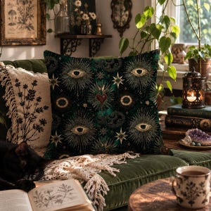 May include: A square throw pillow featuring a dark green background with a repeating pattern of golden eyes, radiant sunbursts, and central hearts. The design includes intricate star motifs and fine lines, creating a detailed celestial and anatomical graphic print across the entire surface of the fabric.