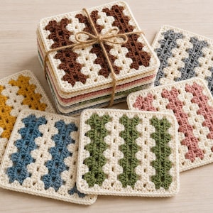 Op de afbeelding: Een set vierkante gehaakte onderzetters met een herhalend patroon van crèmekleurig garen, afgewisseld met diagonale strepen in diverse kleuren zoals bruin, blauw, geel, groen en roze. De onderzetters zijn opgestapeld en samengebonden met touw.