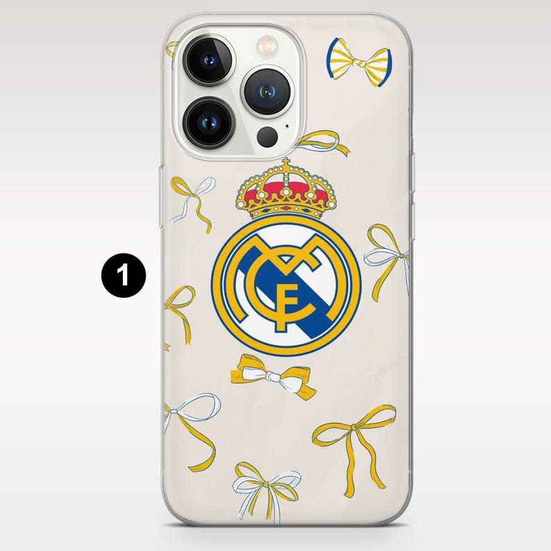 May include: A clear phone case featuring the Real Madrid soccer club logo in the center, topped with a crown. The design is accented with a scattered pattern of small yellow and white bows throughout the background of the protective cover.