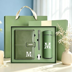May include: A sage green gift set featuring a notebook with a magnetic closure, a metal pen, and a vacuum-insulated tumbler. Each item is personalized with the name Marissa and the letter M in white. The set is presented in a matching green box.