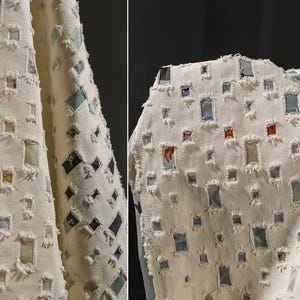 May include: An off-white denim fabric featuring a repeating pattern of rectangular cutouts with frayed edges. Each cutout reveals a different colored fabric patch underneath, including shades of blue, gray, and burnt orange.
