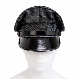 Puede incluir: Una gorra de estilo militar negra con un patrón texturizado de piel de serpiente en la corona y una visera de charol negro brillante. Una banda de charol negro a juego se extiende horizontalmente por la parte delantera, sujeta por pequeños detalles circulares laterales.