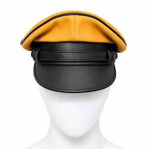 Könnte beinhalten: Eine Mütze im Militärstil mit senfgelber Krone, schwarzer Paspelierung und schwarzem Schirm. Die Vorderseite ist mit einem schwarzen Zierriemen versehen, der an den Seiten mit zwei kleinen schwarzen Knöpfen befestigt ist und eine flache Form hat.