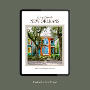 Peut inclure: Une tablette numérique affichant un guide de la ville de La Nouvelle-Orléans avec le texte City Guide NEW ORLEANS et www.jordanmccoytravel.com. L'écran présente une photo de maisons historiques colorées orange, bleues et jaunes, entourées d'arbres.