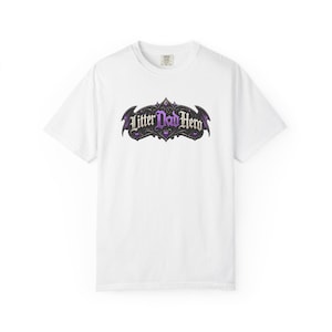Op de afbeelding: Een wit T-shirt met korte mouwen en een centraal grafisch ontwerp met de tekst Litter Dad Hero in een gotisch lettertype. De tekst wordt omringd door een donker, sierlijk, vleugelachtig kader met paarse accenten en kleine hartjes.