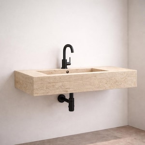 May include: A wall-mounted rectangular bathroom sink crafted from beige travertine stone with a textured, porous surface. It features a matte black faucet and a matching black P-trap drain pipe extending from the underside of the basin.