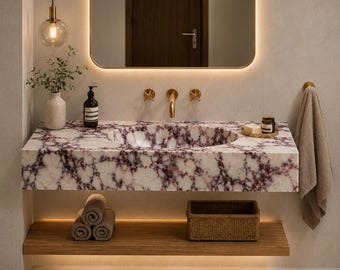 Könnte beinhalten: Ein wandmontierter Waschtisch mit einer Arbeitsplatte aus weißem und dunkelviolettem Marmor mit integriertem ovalem Waschbecken, goldenen Armaturen, einem Holzregal darunter mit gerollten Handtüchern und einem geflochtenen Korb sowie einem Spiegel.