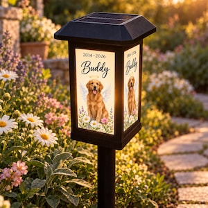 May include: A black solar garden stake light featuring a rectangular illuminated panel with a golden retriever illustration, angel wings, a halo, the name Buddy, and the years 2014-2026 printed above a floral arrangement of daisies and lavender.