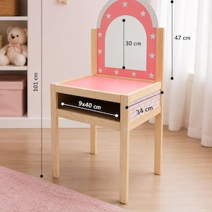 May include: A wooden chair with a pink seat and a pink arched backrest featuring white stars and a central mirror. The chair has a storage compartment under the seat. Dimensions are 101 cm total height, 46 cm width, 47 cm backrest height, 30 cm mirror height, 34 cm depth, and a 9x40 cm storage opening.
