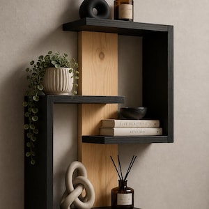 May include: A wall-mounted shelving unit featuring a central vertical light wood panel with three black horizontal shelves. The shelves hold a black vase, a candle, a potted plant, two books titled Live Beautifully and Kinfolk, a bowl, and a diffuser.