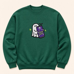 May include: A dark green crewneck sweatshirt featuring an embroidered design of a white ghost holding a purple beverage can. The can displays a skull icon, the text "custom name," and small star accents. A small black bat is positioned above the can.