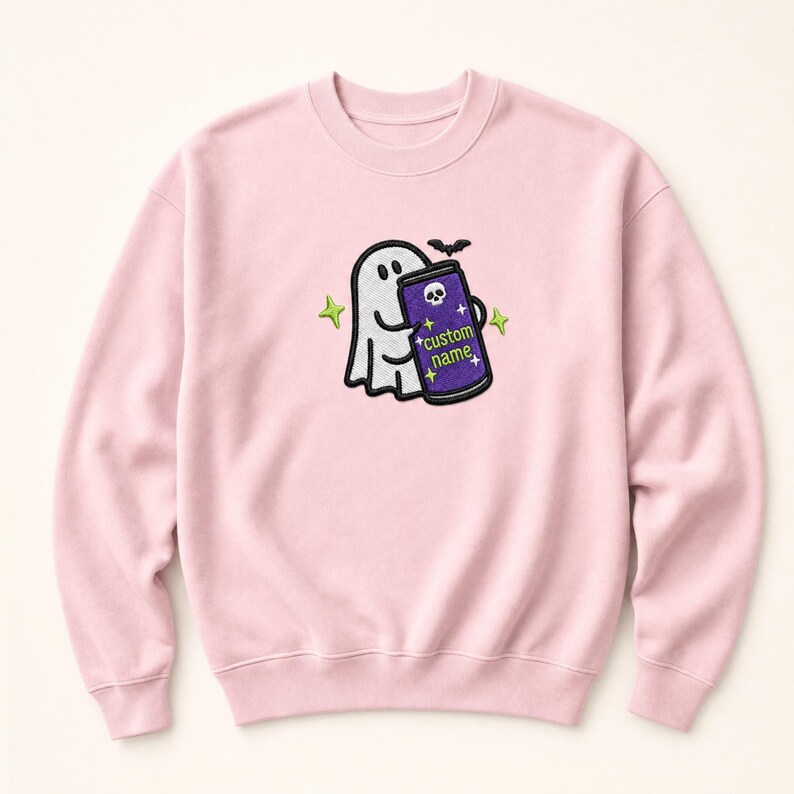 May include: A light pink crewneck sweatshirt featuring an embroidered design of a white ghost holding a purple can with a skull icon and the text custom name. The design includes a small black bat and four lime green four-pointed stars.